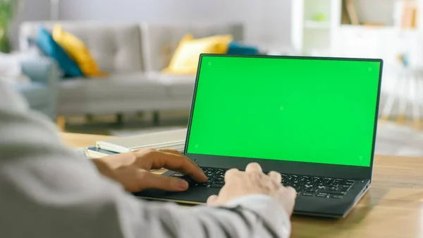 Nahaufnahme eines Mannes, der in seinem gemütlichen Wohnzimmer am Schreibtisch sitzt und Laptop mit grünem Bildschirm benutzt. — Stockfoto