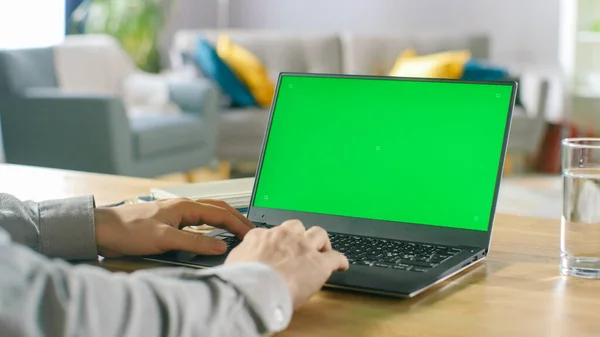 Close-up of a Man Uses Laptop with Green Mock-up Screen Siedząc przy biurku w swoim przytulnym salonie. — Zdjęcie stockowe