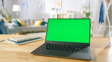 Yeşil Model Ekranlı Modern Laptop Samimi Oturma Odasındaki Masanın Üzerinde Duruyor. Cep telefonu olan adam dinlenmek için sandalyeye oturdu..
