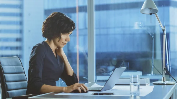 Porträt der schönen Geschäftsfrau bei der Arbeit an einem Laptop in ihrem modernen Büro mit Stadtbild-Fensterblick. Weibliche Führungskräfte nutzen Computer. — Stockfoto