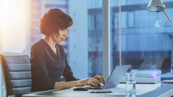 Porträt der schönen Geschäftsfrau bei der Arbeit an einem Laptop in ihrem modernen Büro mit Stadtbild-Fensterblick. Weibliche Führungskräfte nutzen Computer. — Stockfoto