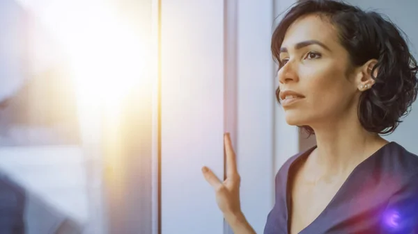 Portret van de mooie jonge zakenvrouw die goed kijkt vanuit haar kantoorraam. Zelfverzekerde en aantrekkelijke Spaanse vrouw die nadenkt over haar business project. — Stockfoto