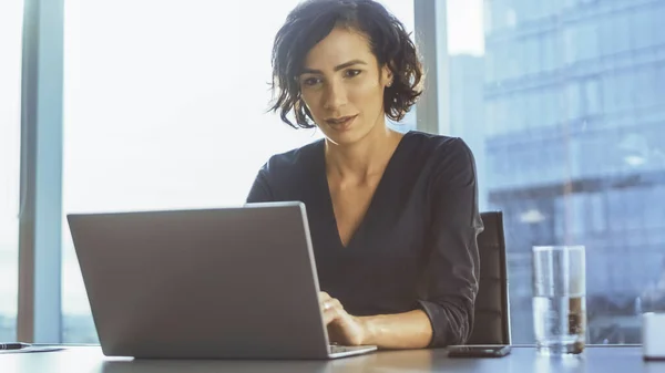 A executiva confiante trabalha em um laptop sentado em sua mesa no escritório moderno com vista para a paisagem urbana da Grandiouse. Busiesswoman usa laptop. — Fotografia de Stock