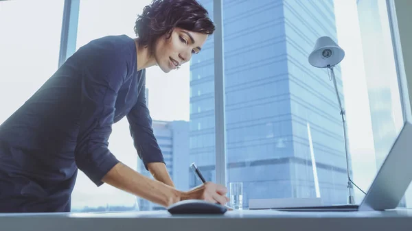 Χαμηλή γωνία Shot of Confident Businesswoman Leans on Her Office Desk, Γράφει πληροφορίες σε έγγραφα και εξετάζει το Laptop. Επιτυχημένη γυναίκα κάνει επιχειρήσεις. — Φωτογραφία Αρχείου