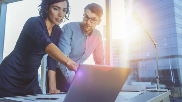 Jeune homme d'affaires prometteur et femme d'affaires discutant de leur projet de démarrage et utilisant un ordinateur portable. Nouvelle génération de jeunes gens intelligents en affaires. Flare du soleil derrière eux. — Photo