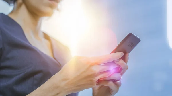 Detailní záběr stylové podnikatelky pomocí chytrého telefonu. Zaměření mobilního telefonu. Světlice za ní. — Stock fotografie
