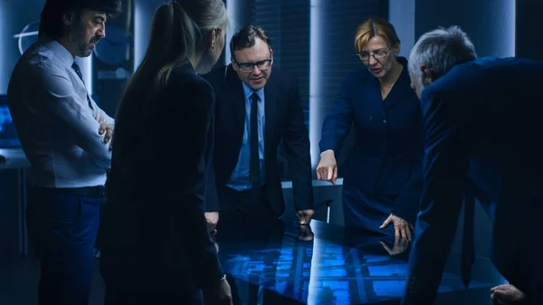 Diverse Team of Government Intelligence Agents standing Around Digital Touch Screen Table and Tracking Suspect, senior officer does Interactive Gesturing. Big Dark Surveillance Room. — Stock fotografie
