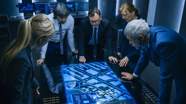 Висококутний знімок команди урядових агентів розвідки, що розмовляють, стоячи навколо цифрового сенсорного екрану таблиці та відстежуючи підозрюваного. Операція супутникового спостереження в моніторингу . — стокове фото