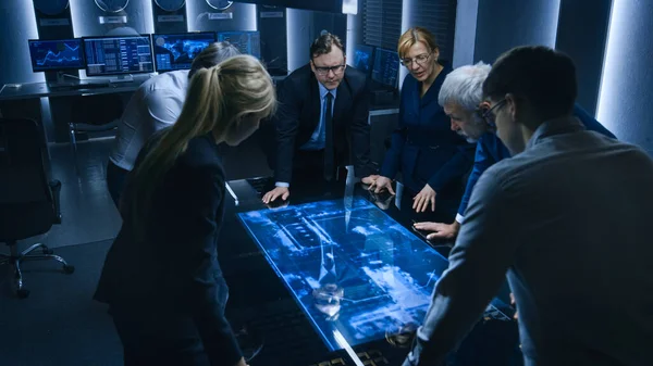 Team of Government Intelligence FBI Agents standing Around Digital Touch Screen Table and Tracking Suspect Vehicle Using Satellite Surveillance in the Monitoring Room. — Stock fotografie