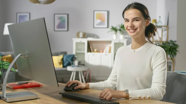 Retrato de la hermosa joven que trabaja en el ordenador personal de su acogedora sala de estar. Ella sonríe encantadoramente mirando a la cámara. —  Fotos de Stock