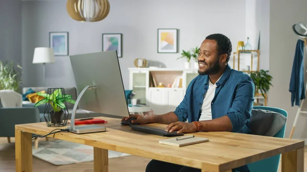 Happy Young Man λαμβάνει χώρα στο γραφείο του και αρχίζει να εργάζεται σε έναν προσωπικό υπολογιστή. Στο φόντο άνετο σαλόνι. — Φωτογραφία Αρχείου