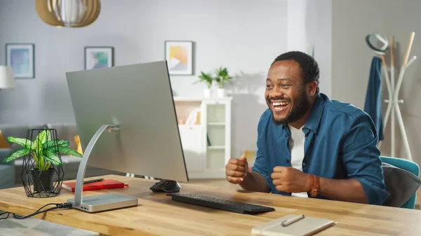 Happy Young Man Uses Personal Computer at Home, Laughing at Funny Video. In the Background Cozy Living Room.