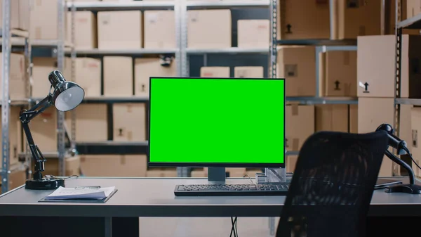 Aufnahme eines Lagerbestandsverwalters am Schreibtisch und eines Personal Computers mit geöffneter Kalkulation. Im Hintergrund Regale voller versandfertiger Kartonverpackungen. — Stockfoto