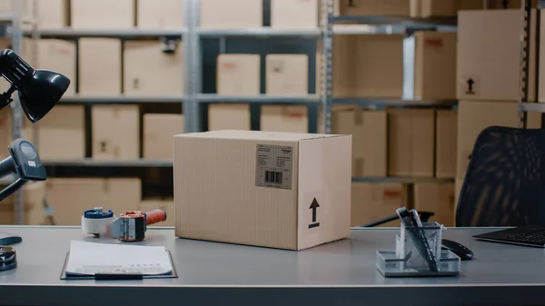 Cardboard Box Package Standing on the Table of the Warehouse where Rows of Shelves with Parcels Waiting to be Shipped and Delivered. — Stock Photo, Image