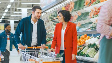 Süpermarkette: Mutlu Genç Çift Mağazanın Taze Üretim Bölümü 'nden Organik Sebzeleri Seçiyor. Sevgilisi alışveriş arabasını iterken, kız arkadaşı bakkaldan yiyecek alıyor..