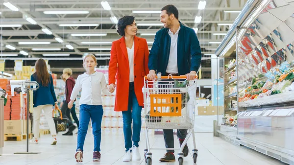 At the Supermarket: Happy Family of Three, Holding Hands, Walks Through Fresh Produce Section of the Store. Father, Mother and Daughter Having Fun Time Shopping.