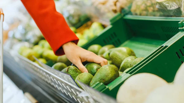 V supermarketu: Detailní záběr na ženy, jak berou avokádo z čerstvě vyrobené sekce a umístí ho do nákupního košíku. — Stock fotografie