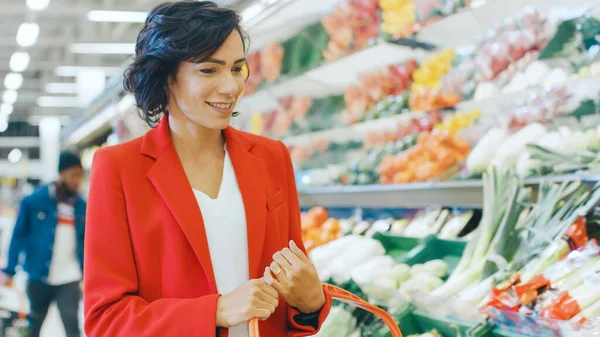 V supermarketu: Portrét krásné usmívající se ženy výběr produktů v sekci čerstvé produkce a umístěte je do nákupního košíku. — Stock fotografie