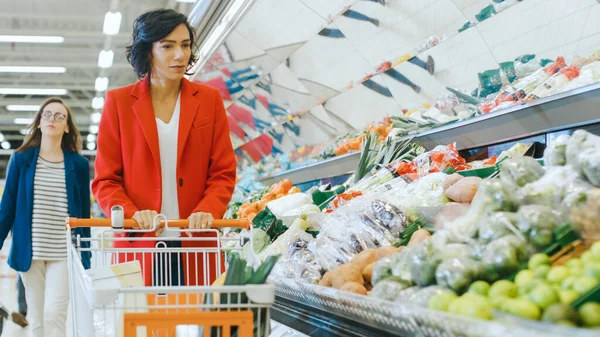 A szupermarketben: lövés egy gyönyörű fiatal nő sétál át a friss termékek részleg, kiválasztása zöldségek. — Stock Fotó