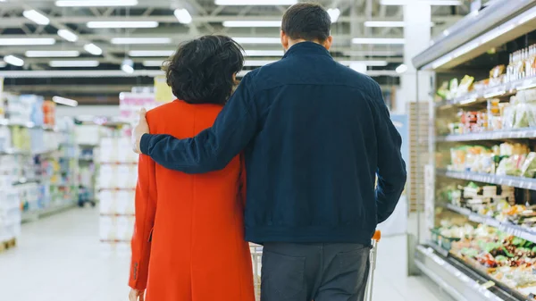 Al supermercato: Happy Young Couple cammina attraverso la sezione dei prodotti freschi del negozio, Man abbraccia amorevolmente la donna. Colpo alla vista posteriore. — Foto Stock