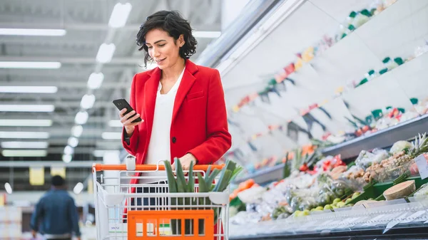 Στο supermarket: Beautiful Young Woman Χρησιμοποιεί Smartphone Ενώ Στέκεται στο τμήμα Fresh Produce του καταστήματος. — Φωτογραφία Αρχείου