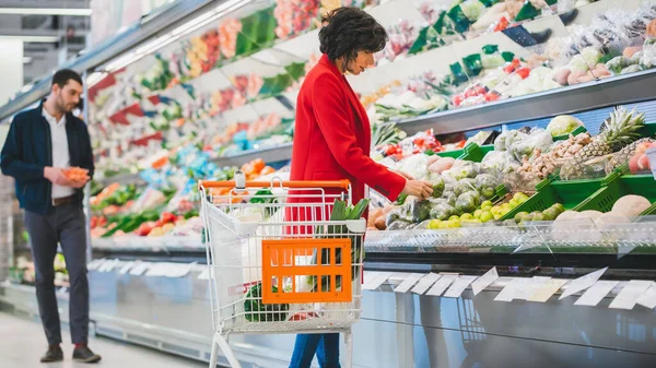 У супермаркеті: красива молода жінка проходить через секцію свіжих продуктів, вибирає фрукти та овочі. покупки фруктів і овочів в магазині . — стокове фото