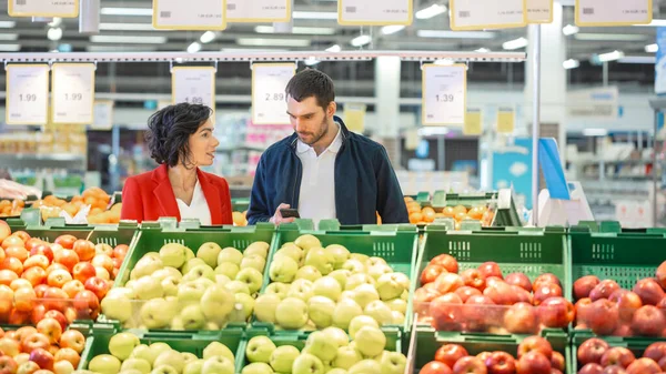 En el supermercado: Feliz pareja joven elige verduras orgánicas en la sección de productos frescos de la tienda. Novio y novia recogiendo alimentos juntos. — Foto de Stock