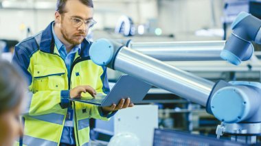 Fabrikada: Otomasyon Mühendisi Robotik Kol Programı için Dizüstü bilgisayar kullanıyor. Otomatik Üretim Endüstrisinde Yeni Dönem.