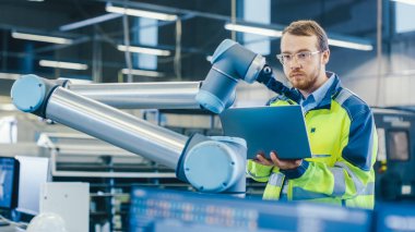 Fabrikada: Otomasyon Mühendisi Robotik Kol Programı için Dizüstü bilgisayar kullanıyor. Otomatik Üretim Endüstrisinde Yeni Dönem.