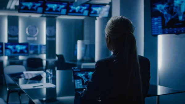 La agente especial femenina trabaja en una computadora portátil en segundo plano. La agente especial a cargo habla con el militar en la sala de monitoreo. En el centro de control del sistema ocupado de fondo con monitores que muestran el flujo de datos. — Foto de Stock