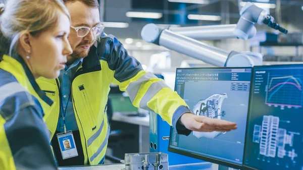 À l'usine : Un ingénieur mécanicien et une ingénieure en chef travaillent ensemble sur l'ordinateur personnel, ils discutent des détails du modèle de moteur 3D pour bras robotique. — Photo