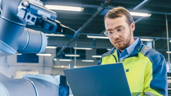 V továrně: Automation Engineer používá notebook pro programování robotické rameno. Nová éra automatického zpracovatelského průmyslu. — Stock fotografie