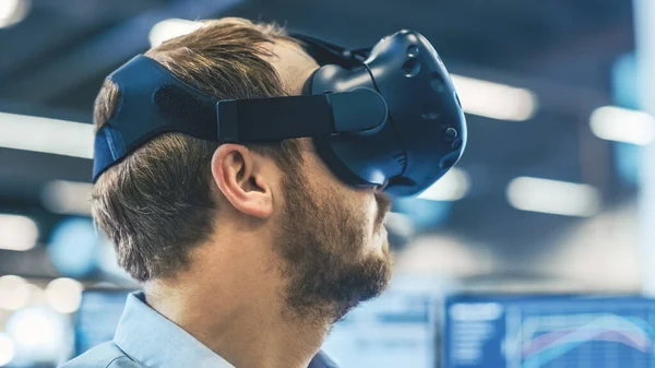 Retrato del ingeniero industrial con auriculares de realidad virtual y gestos con controladores. En el fondo fuera de foco muestra y planta de fabricación. —  Fotos de Stock