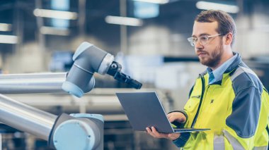 Fabrikada: Otomasyon Mühendisi Robotik Kol Programı için Dizüstü bilgisayar kullanıyor. Otomatik Üretim Endüstrisinde Yeni Dönem.