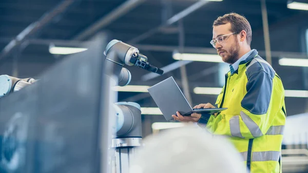 Na Fábrica: Engenheiro de Automação Usa Laptop para Programação de Braço Robótico. Nova era na indústria de fabricação automática. — Fotografia de Stock