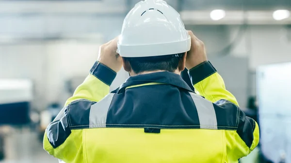 Tillbaka Visa Skott av industriingenjören bär skyddande kläder Puts på hårt hatt och går genom modern tillverkning anläggning med automatiserade maskiner som arbetar i bakgrunden. — Stockfoto