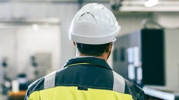 Tillbaka Visa Skott av industriingenjören bär skyddande kläder promenader genom modern tillverkningsanläggning med automatiska maskiner som arbetar i bakgrunden. — Stockfoto