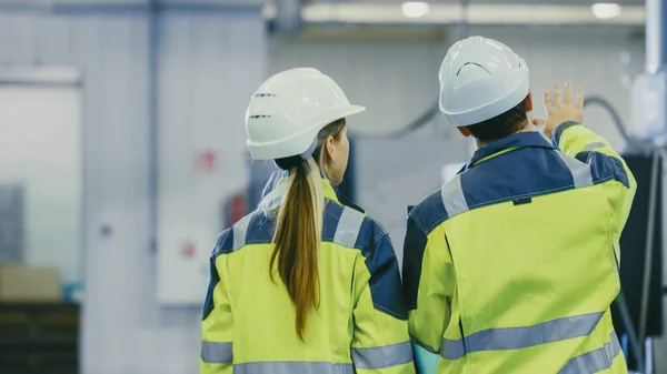 男产业工人和女首席机械工程师在步行通过制造厂，同时讨论工厂的新项目。有工作机制的设施. — 图库照片