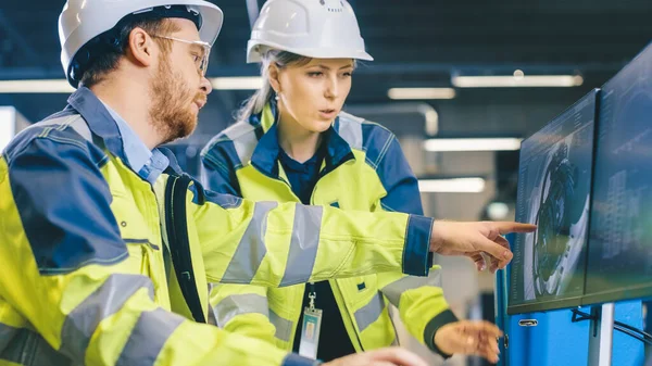 À l'intérieur de l'usine, un ingénieur mécanique masculin et une ingénieure en chef travaillent ensemble sur l'ordinateur personnel, ils discutent des détails de la conception du modèle de moteur 3D. — Photo