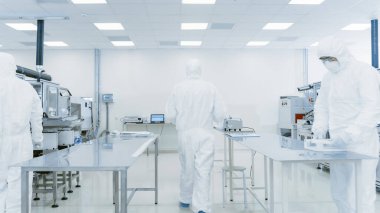 Koruyucu Takım Elbise Bilimadamı Laboratuvardan Bitmiş Ürün Kutusunu Taşıyor. Modern Endüstriyel Makineler Tesisindeki İşçiler. Ürün Üretim Süreci: İlaç, Yarı iletkenler