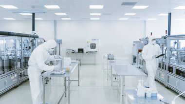 Kalite Kontrol: Dijital Tablet Bilgisayar kullanan ve koruyucu giyimli bilim adamı imalat laboratuarından geçiyor. Ürün Üretimi: İlaç, Yarı iletkenler, Biyoteknoloji.