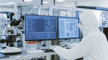 Kişisel Bilgisayarda Araştırma Yapan Koruyucu Giysiler Bilimadamının Omuz Görünümü Üzerindeki Laboratuvarda. Modern Manufactory Yarı iletkenler ve İlaç Ürünleri Üretimi.