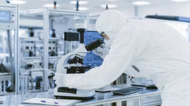Koruyucu Giysiler Laboratuvarında Araştırma Yapan Bilimadamı Mikroskop ve Kişisel Bilgisayar kullanır. Modern Manufactory Yarı iletkenler ve İlaç Ürünleri Üretimi.