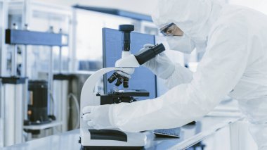 Koruyucu Giysiler Laboratuvarında Araştırma Yapan Bilimadamı Mikroskop ve Kişisel Bilgisayar kullanır. Modern Manufactory Yarı iletkenler ve İlaç Ürünleri Üretimi.