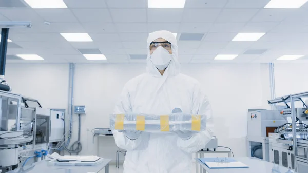 Científico en traje protector lleva el caso con el producto terminado a través del laboratorio. Instalación con maquinaria industrial moderna. Proceso de fabricación de productos: productos farmacéuticos, semiconductores —  Fotos de Stock