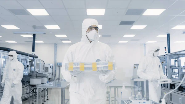 Scientist in Protective Suit Carries Case with Finished Product Through Laboratory. Facility with Modern Industrial Machinery. Product Manufacturing Process: Pharmaceutics, Semiconductors