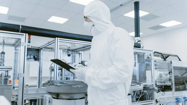 品質管理チェック:デジタルタブレットコンピュータを使用して保護スーツを身に着けている科学者は製造研究所を通って歩く。製品製造:医薬品、半導体、バイオテクノロジー. — ストック写真