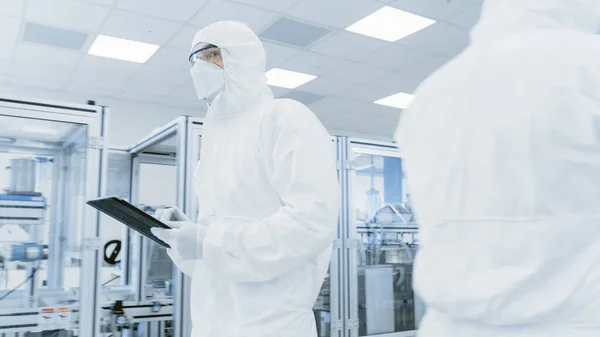 품질 관리 검사: 과학자들이 디지털 태블릿 컴퓨터를 사용하여 보호용 슈트를 입고 제조 연구소를 통해 걸어 다닌다. 제품 제조: 의약품, 반도체, 생물 공학. — 스톡 사진