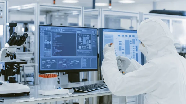 In Laboratory Over the Shoulder View of Scientist in Protective Clothes Holding Test Tube and Doing Research on Personal Computer. Manifattura moderna che produce semiconduttori e articoli farmaceutici — Foto Stock