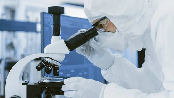 一位穿着防护服的科学家的特写镜头在抛物线中使用显微镜进行研究。现代手工生产半导体和药品. — 图库照片